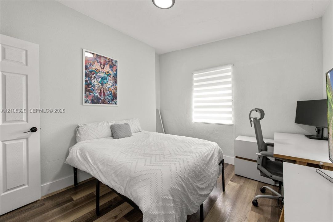 Room featuring wood-finish flooring, a multi-panel door with matte black hardware, and a window with integrated light-filtering shade