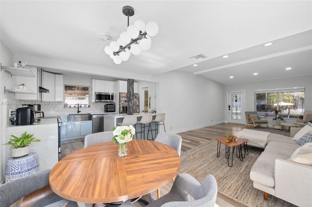 Kitchen featuring white shaker-style cabinetry, quartz countertops, a farmhouse-style sink, and a modern multi-globe chandelier, complemented by wood-finish flooring throughout the space