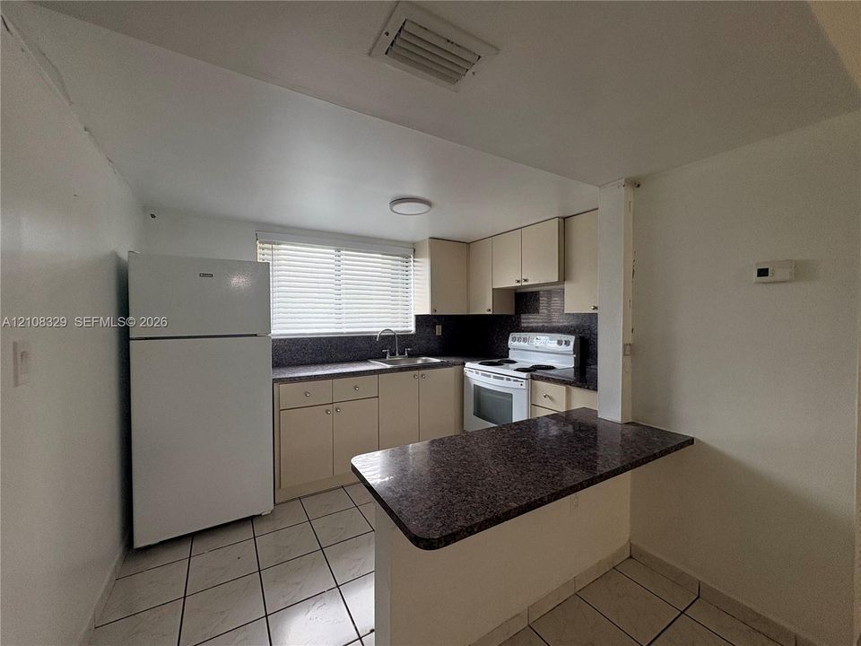 Kitchen featuring a peninsula with a dark countertop, white cabinetry, a top-mount sink, and tiled flooring