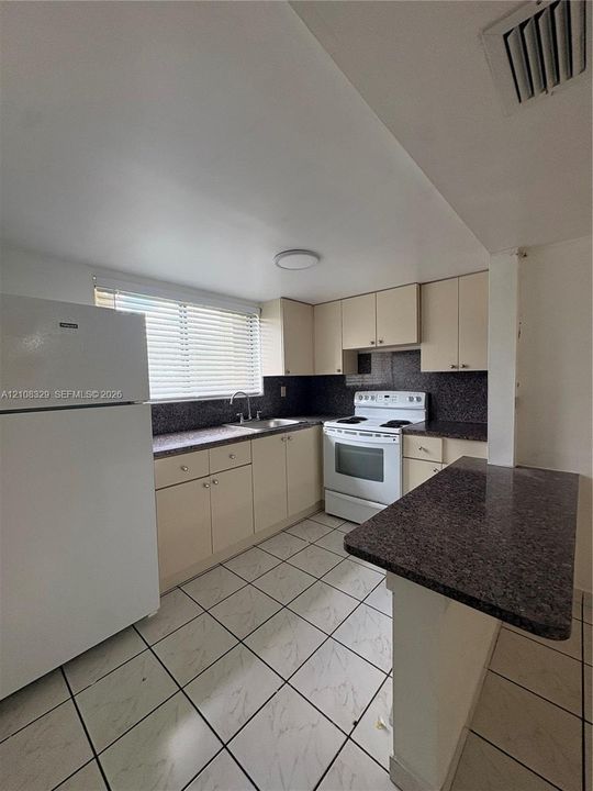 Kitchen featuring light-toned cabinetry, dark solid-surface countertops, tile flooring, and an attached breakfast bar