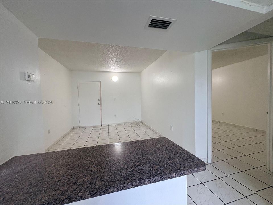 Interior space featuring neutral wall tones, white ceramic tile flooring throughout, and a stone-surface peninsula countertop