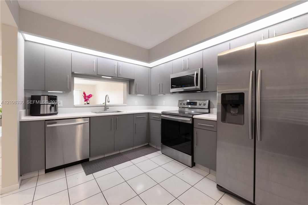 Kitchen featuring flat-panel gray cabinetry, white solid-surface countertops, stainless steel appliances, recessed lighting, and white tile flooring