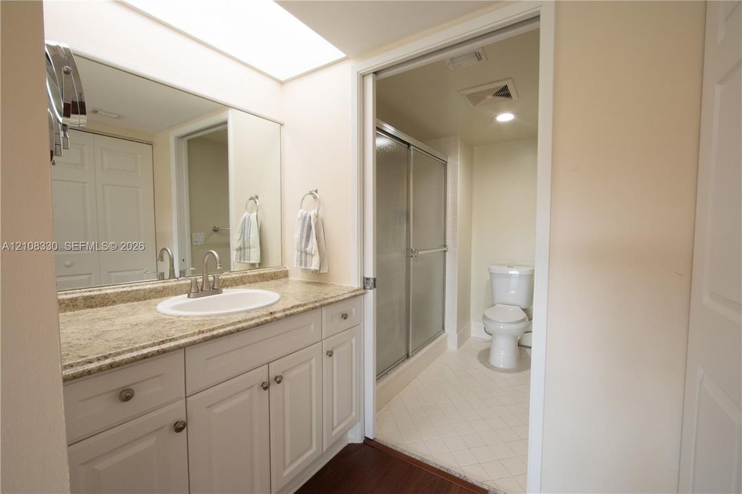 Bathroom featuring a vanity with a stone-finish countertop, oval undermount sink, white cabinetry, a large wall-mounted mirror, and a walk-in shower with sliding glass doors