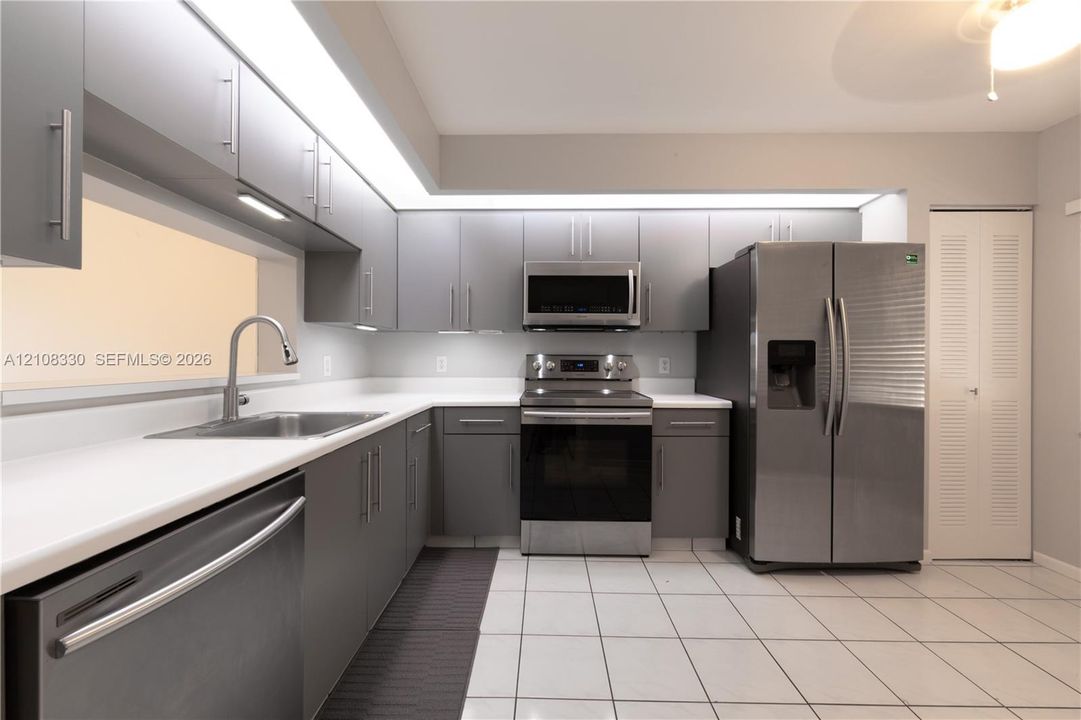 Kitchen featuring gray flat-panel cabinetry, stainless steel appliances, solid surface countertops, recessed lighting, and tile flooring