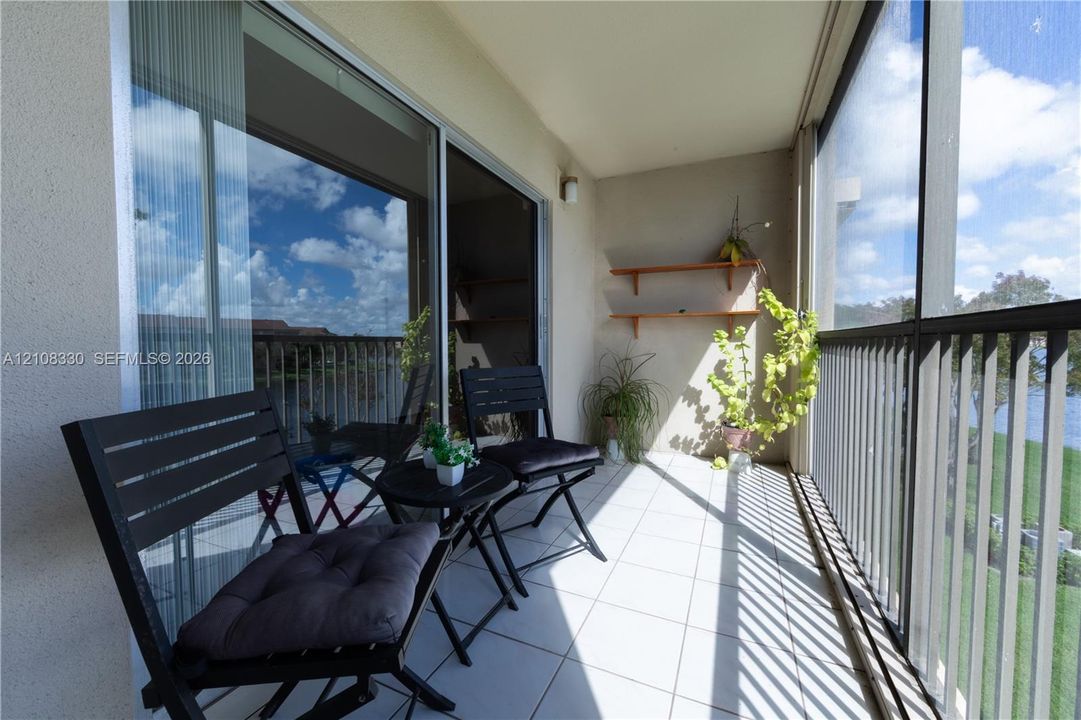 Screened balcony featuring white floor tiling, metal railing, wall-mounted shelving, and sliding glass doors