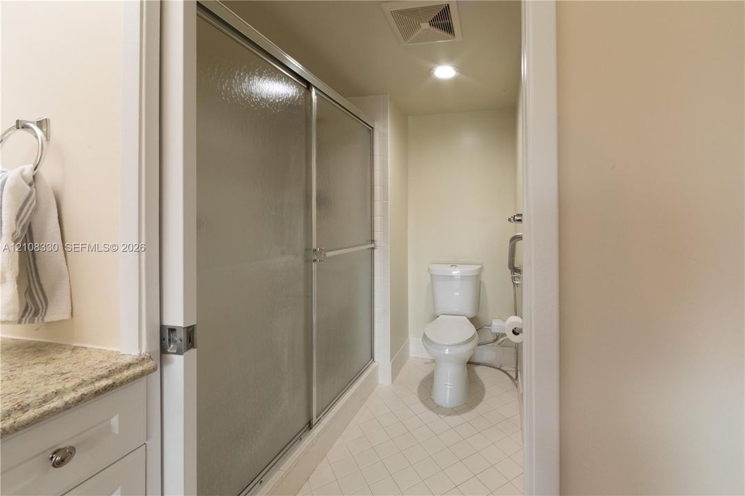 Bathroom featuring a walk-in shower with sliding glass enclosure, stone-finish countertop, white cabinetry, and tile flooring
