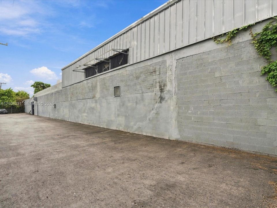 Industrial exterior featuring a concrete masonry unit wall, corrugated metal siding, and a paved asphalt surface