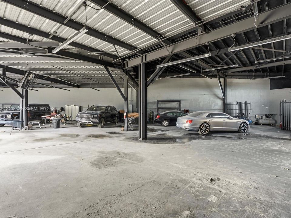 Expansive industrial-style garage featuring exposed steel beam framing, a high-clearance metal roof, concrete flooring, and overhead lighting fixtures