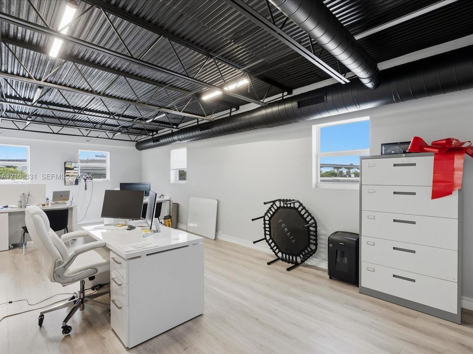 Open-concept room featuring a corrugated metal ceiling with exposed black industrial ducting, wood-finish flooring, and multiple exterior-facing windows