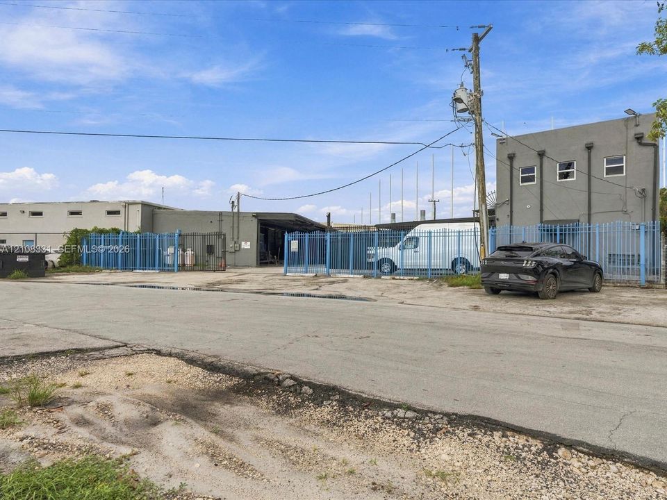 Industrial exterior featuring concrete block construction, paved asphalt lot, and perimeter security fencing with gated access