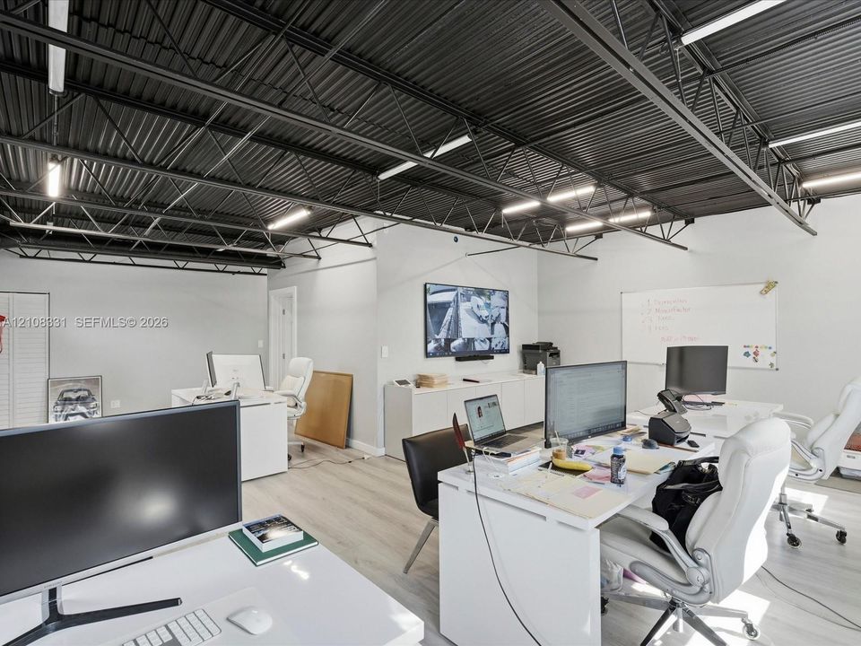 Industrial-style room featuring an exposed black metal ceiling, linear LED lighting, wood-finish flooring, and built-in white cabinetry