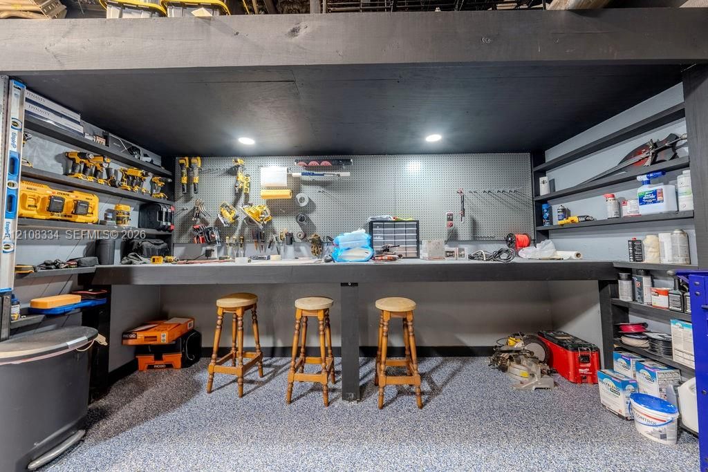 Dedicated workspace featuring a wall-mounted pegboard, integrated recessed lighting, expansive built-in shelving, and epoxy-finish flooring