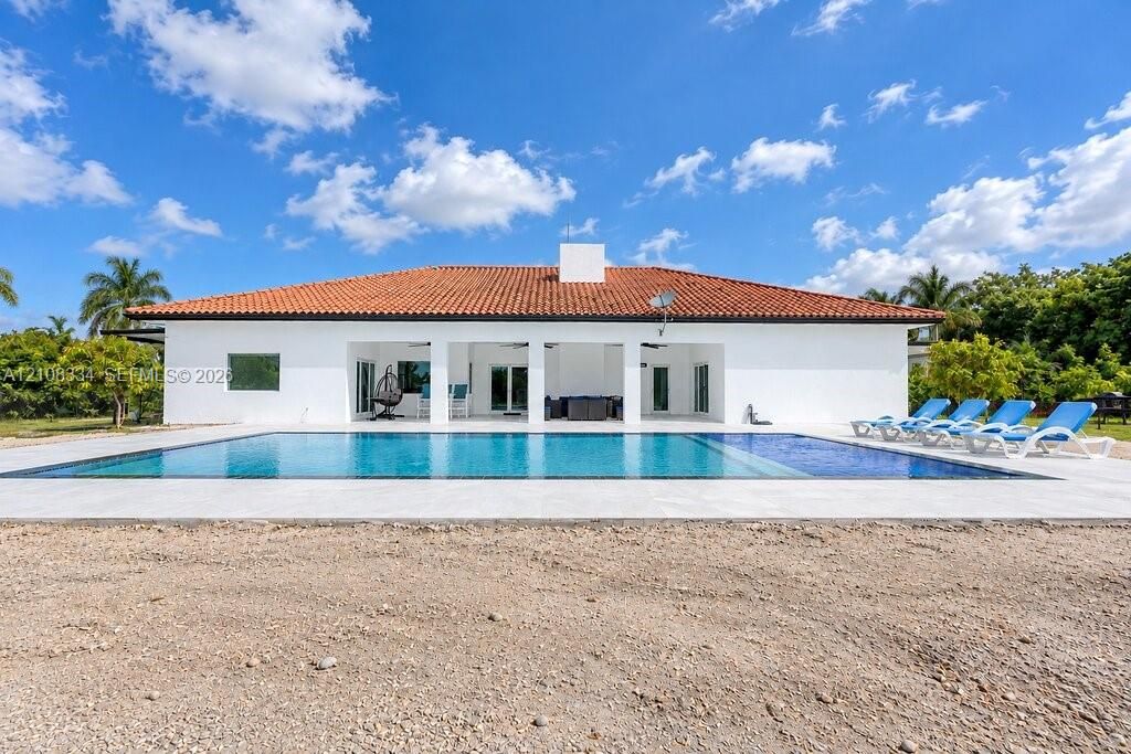 Exterior facade featuring a terracotta-tiled hip roof, expansive rectangular swimming pool, and a covered patio with structural support pillars