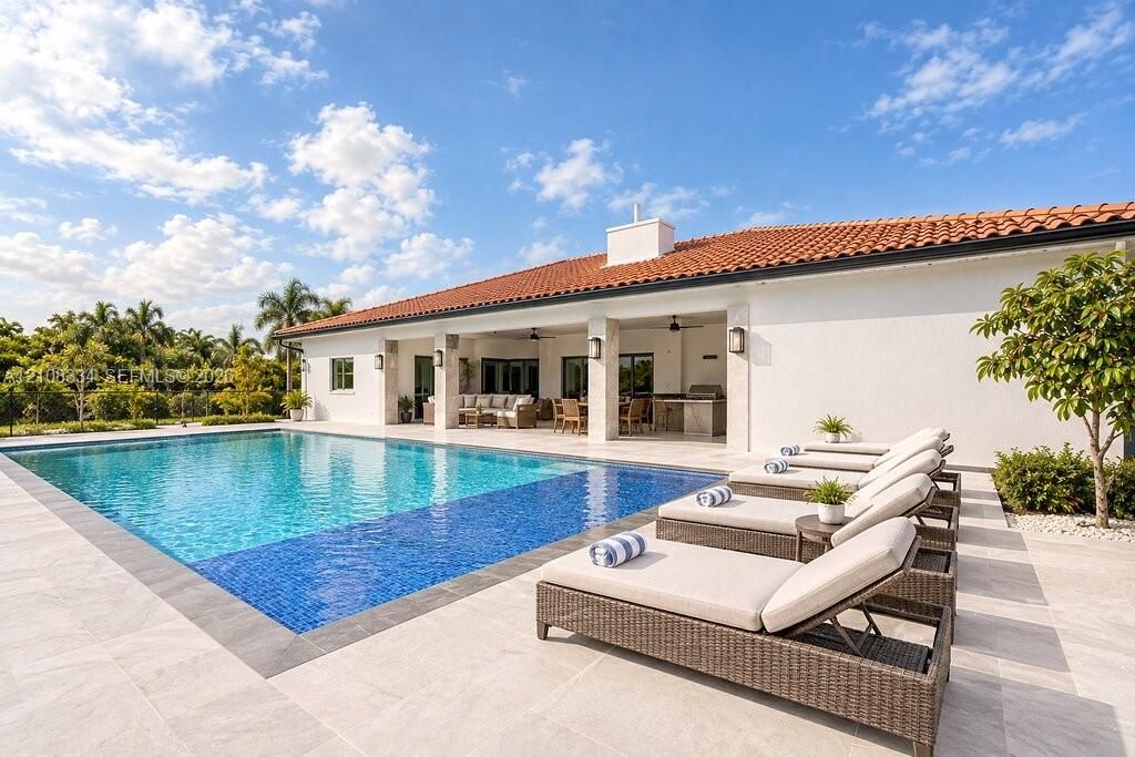 Outdoor living area featuring a covered lanai with stone pillars, an inground pool with tile border, and expansive stone-finish decking