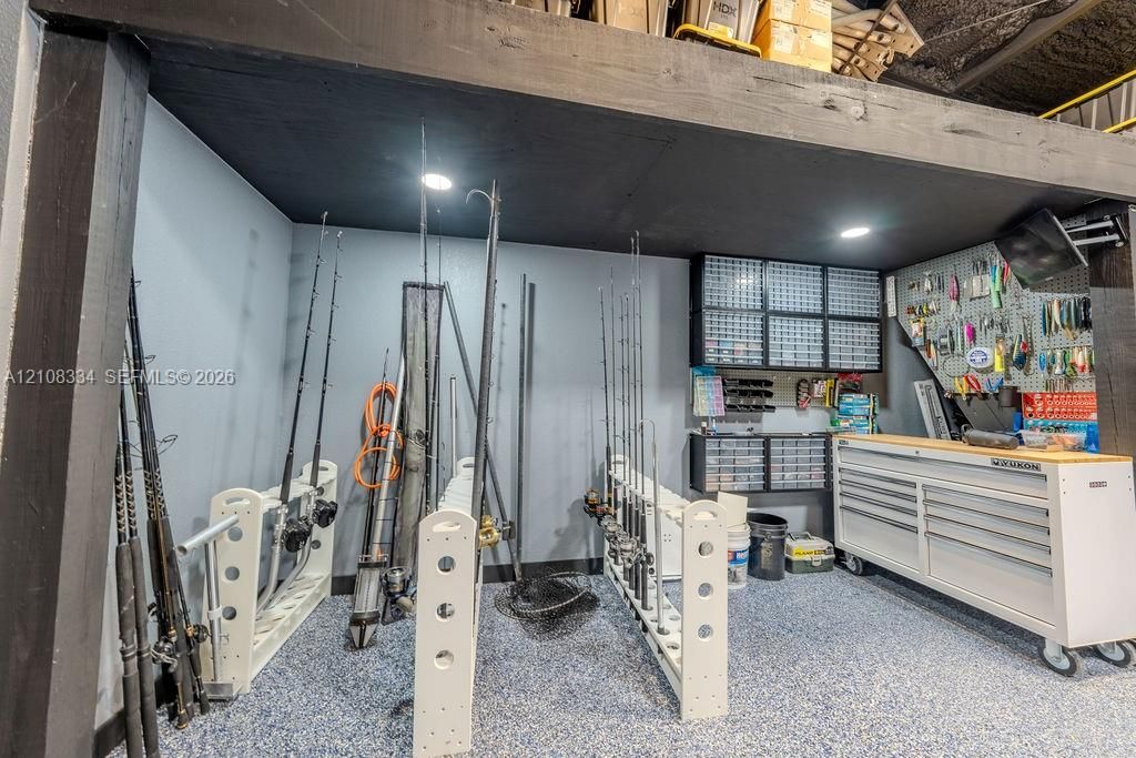 Dedicated workspace featuring overhead recessed lighting, dark painted ceiling beams, epoxy-finished flooring, wall-mounted storage cabinetry, and perforated board organization