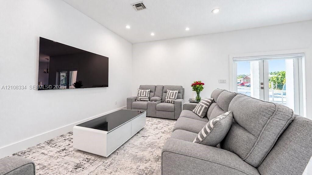 Neutral color palette featuring recessed lighting, a wall-mounted display, and glass-paned exterior doors