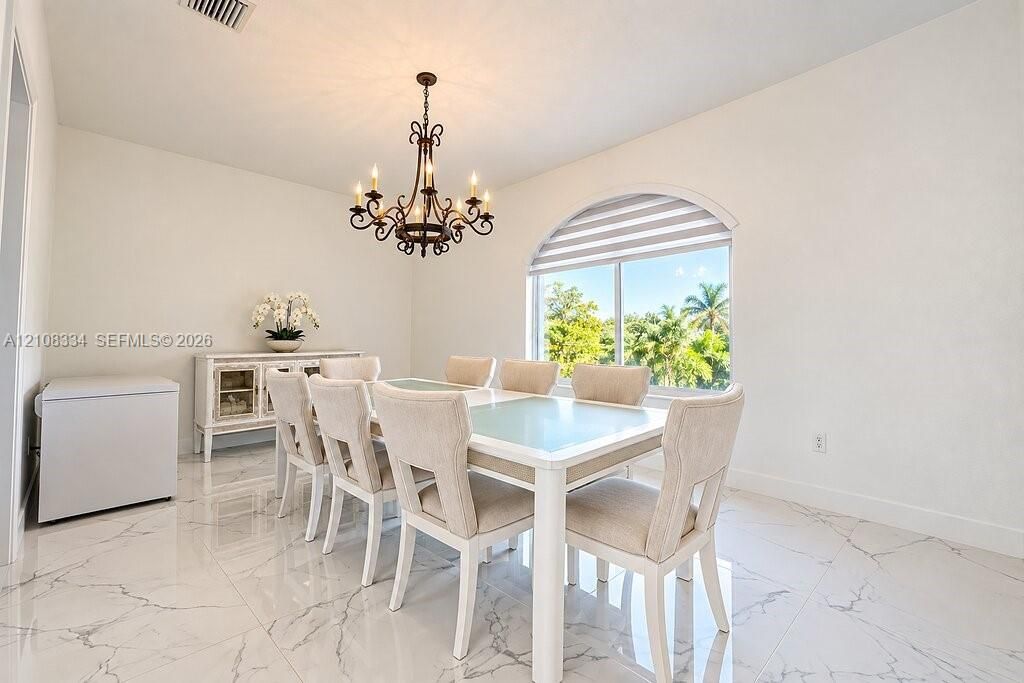 Dining area featuring large-format stone-patterned floor tile, an ornate wrought-iron chandelier, and a prominent arched window with a roller shade