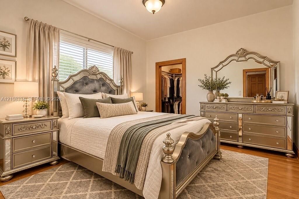 Bedroom featuring wood-finish flooring, a double-hung window with blinds, and a built-in walk-in closet with natural wood trim