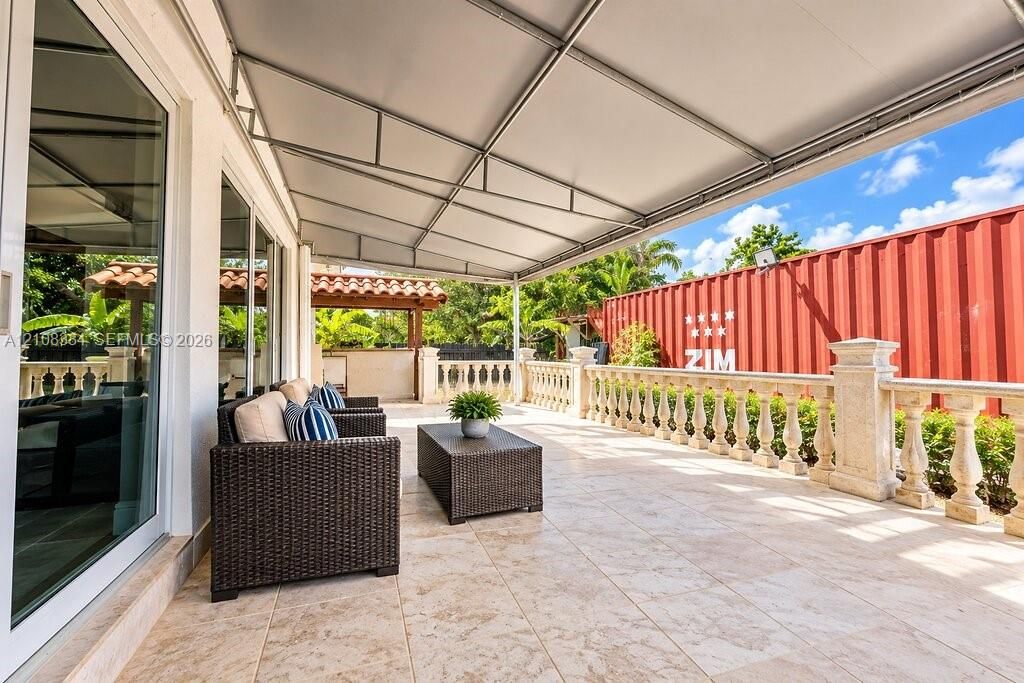 Covered terrace featuring stone-finish floor tiling, ornate stone balustrade railing, and a retractable metal-frame awning