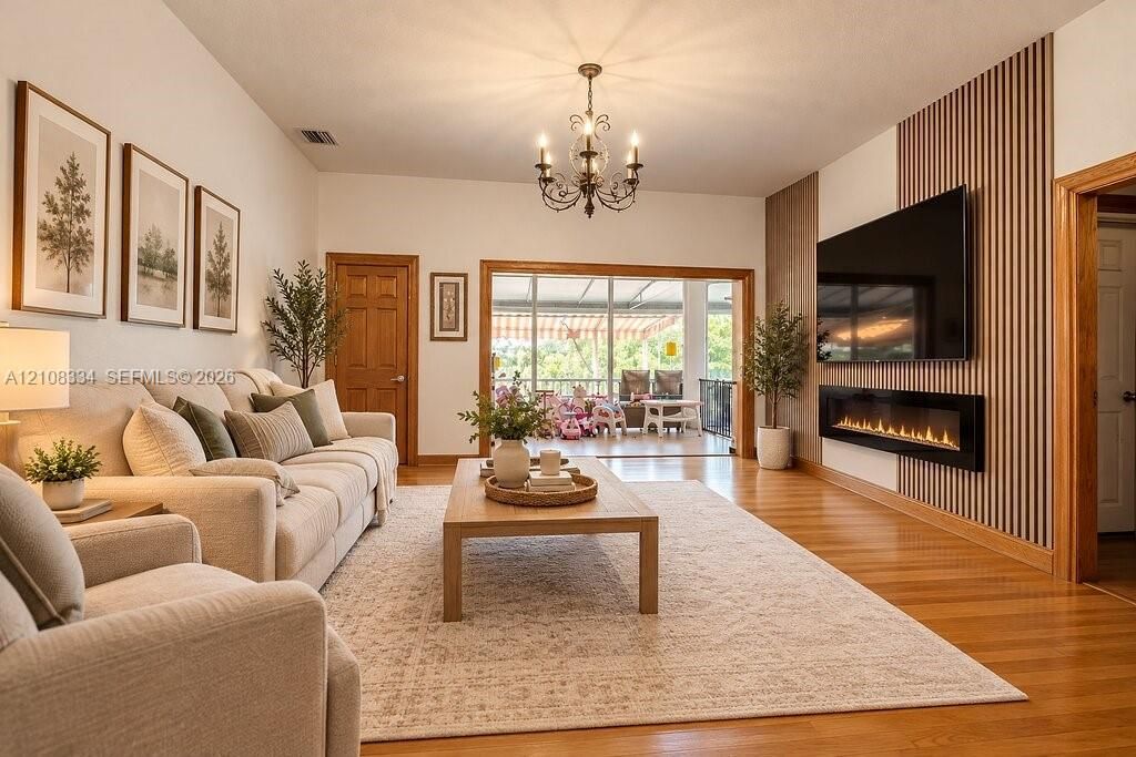 Living area featuring wood-finish flooring, a linear wall-mounted electric fireplace, vertical slat wood wall paneling, and a multi-arm chandelier