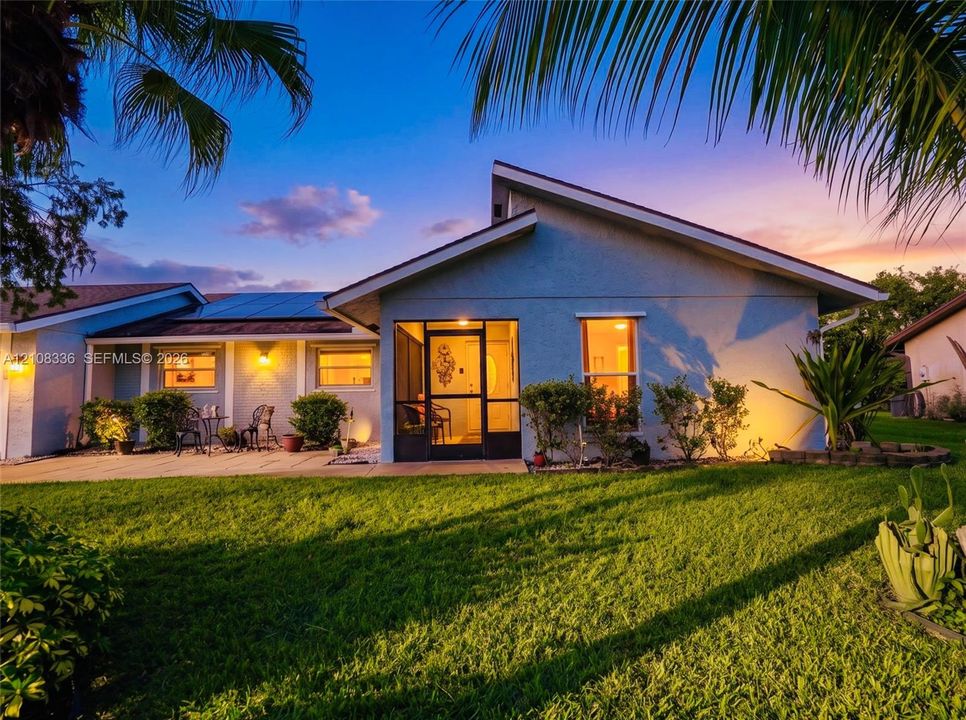 Single-story exterior featuring a screened-in entry, roof-integrated solar panels, stucco siding, and a paved patio area