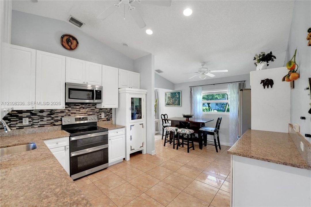 Kitchen featuring white cabinetry, stone-finish countertops, stainless steel appliances, multi-toned mosaic tile backsplash, and ceramic tile flooring