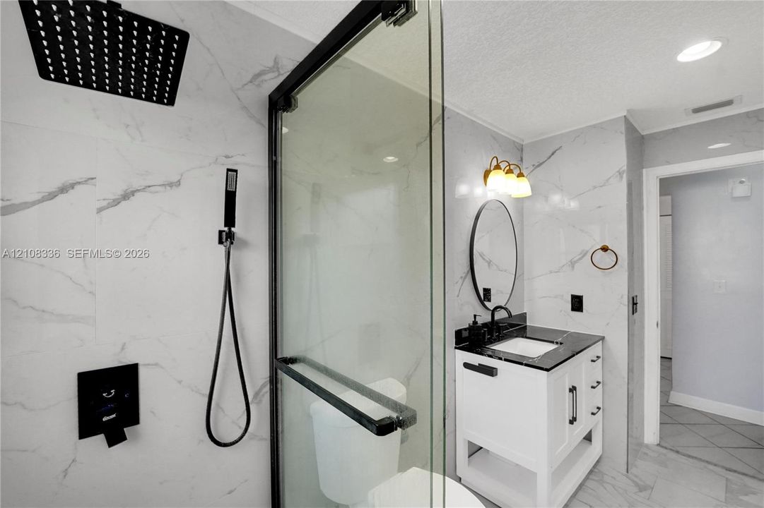 Walk-in shower featuring floor-to-ceiling stone-pattern tile, a rainfall showerhead with handheld attachment, and a black-framed glass enclosure