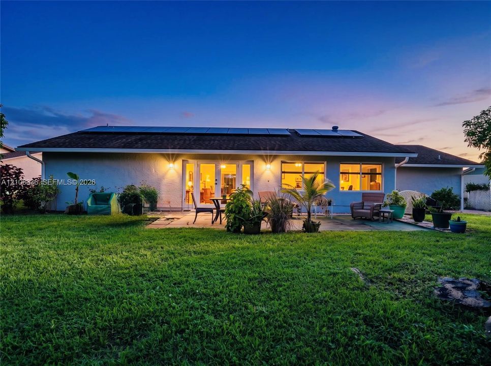 Single-story exterior featuring a concrete patio, roof-mounted solar panels, and large glass French doors