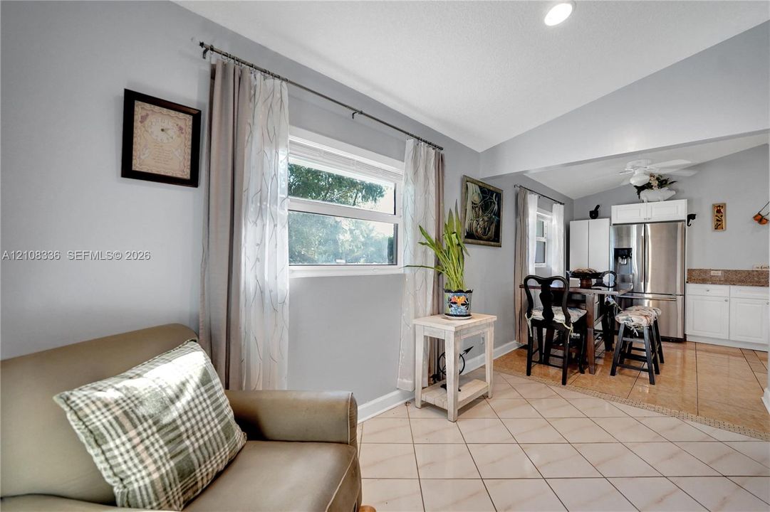 Open-concept interior featuring light-toned diagonal tile flooring, vaulted ceilings, recessed lighting, and white kitchen cabinetry with stainless steel appliances