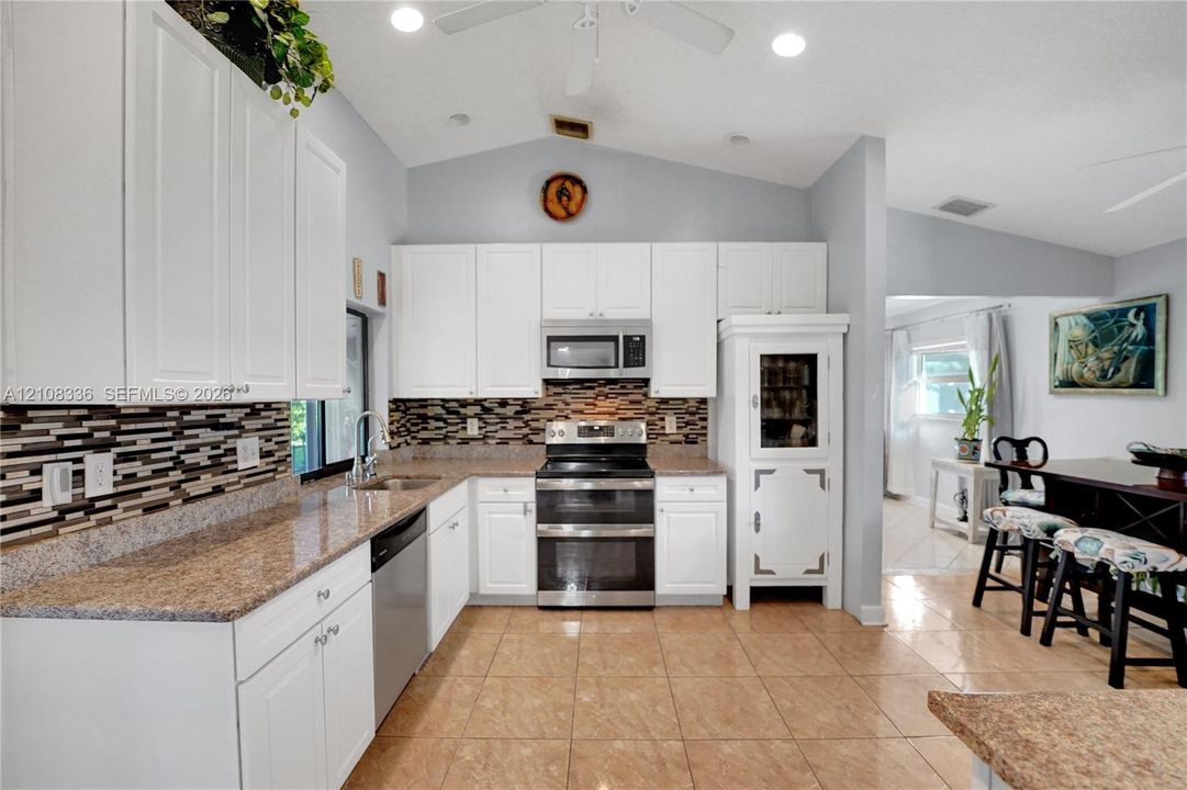 Kitchen featuring white cabinetry, stone-finish countertops, mosaic tile backsplash, stainless steel appliances, and tile flooring under a vaulted ceiling