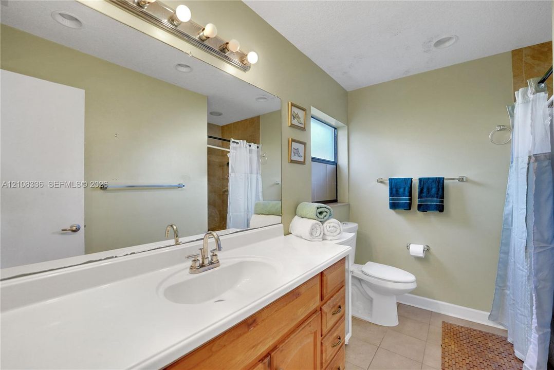 Bathroom featuring a wood vanity with an integrated countertop sink, wall-spanning mirror, multi-bulb vanity light, and tiled flooring