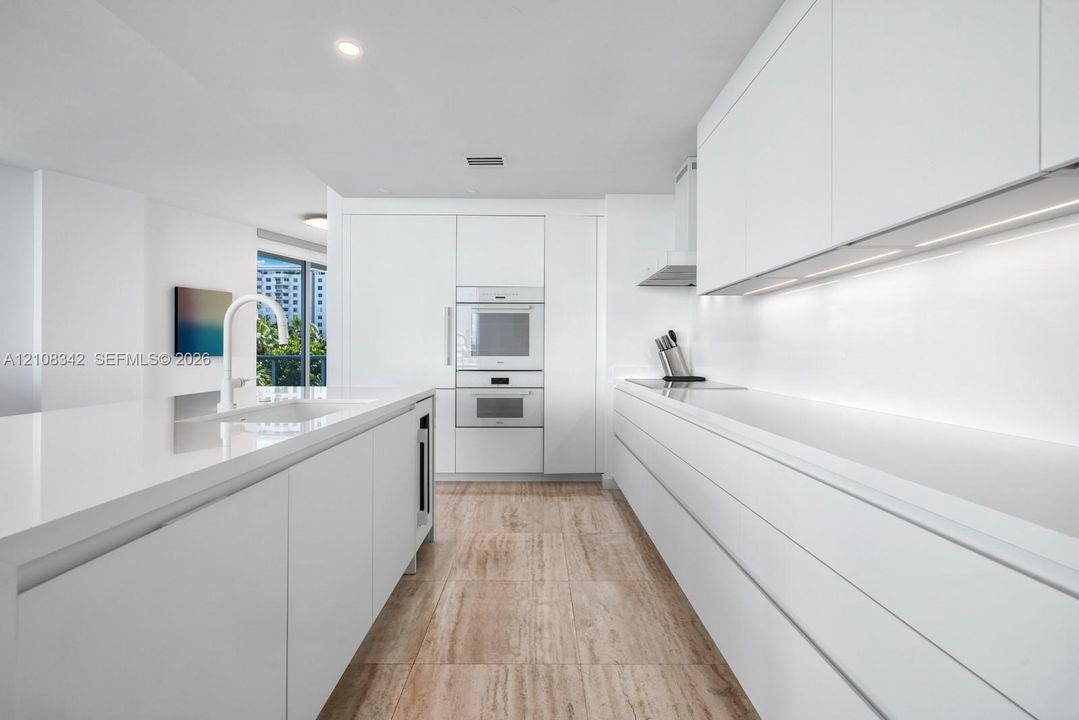 Minimalist kitchen featuring flat-panel cabinetry, white stone-surface countertops, built-in wall ovens, stone-finish flooring, and recessed ceiling lighting