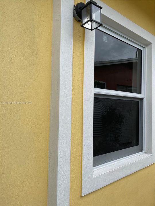Textured exterior stucco finish with white trim framing and attached outdoor lantern-style light fixture