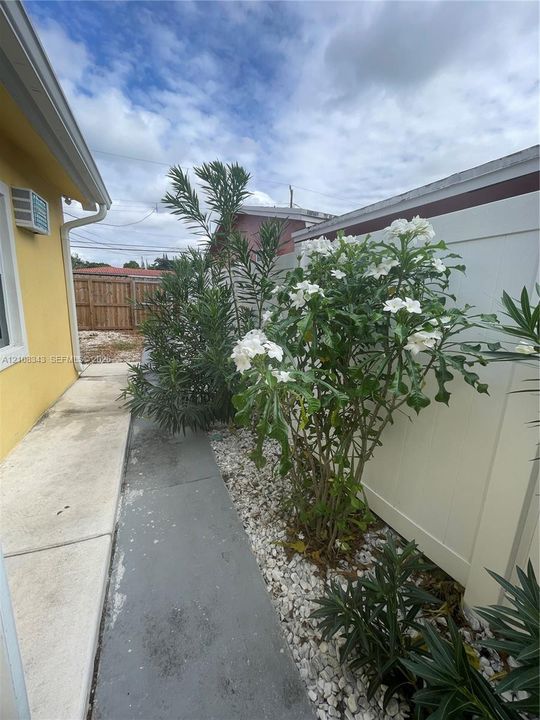 Side yard featuring a poured concrete walkway, white vinyl fencing, and decorative stone landscaping with flowering shrubs