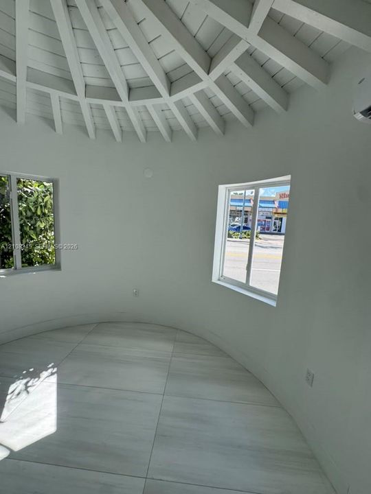 Circular room featuring exposed wood-beam vaulted ceilings, light-tone tile flooring, and sliding windows