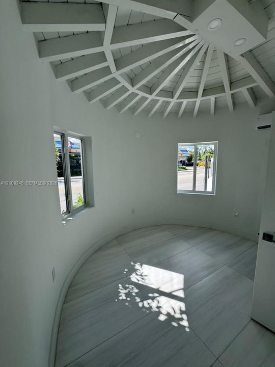 Circular room featuring a vaulted, radial-beam ceiling, wood-finish tile flooring, recessed lighting, and multiple windows