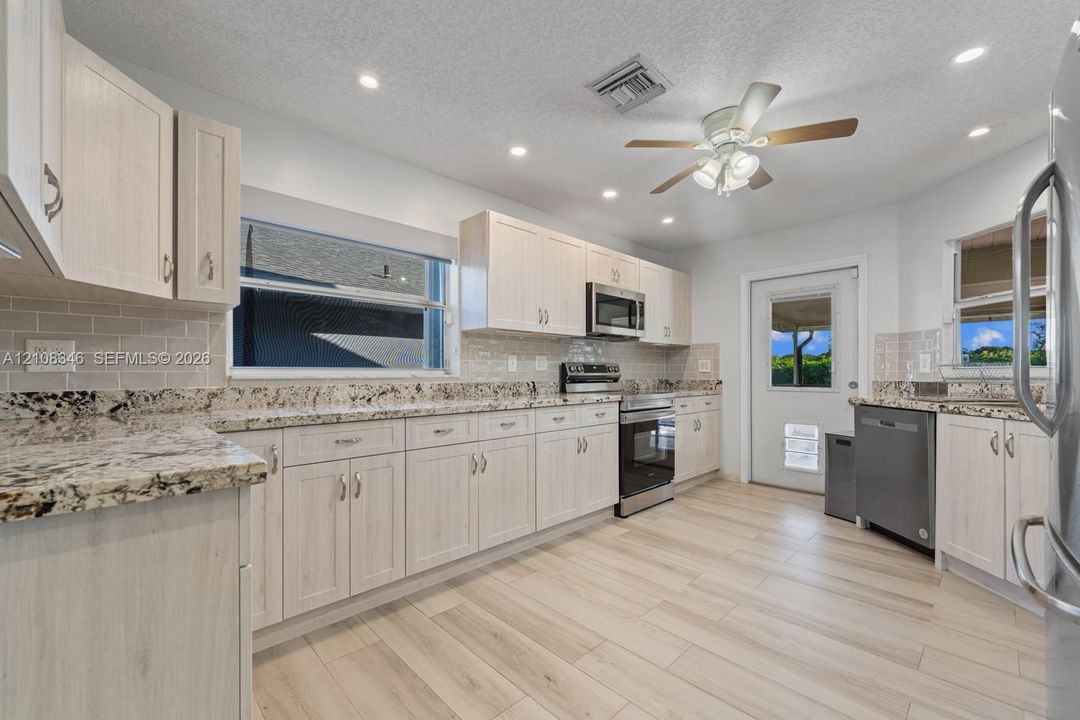 Kitchen featuring light-toned cabinetry, stone countertops, subway tile backsplash, stainless steel appliances, and wood-tile flooring