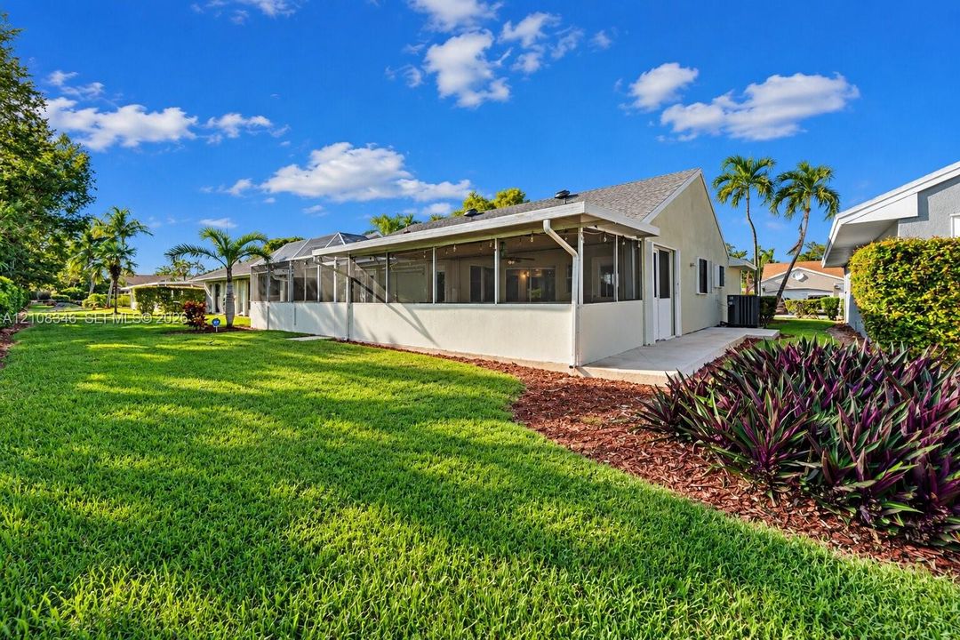 Exterior rear elevation featuring a screened-in lanai, concrete patio, expansive lawn, mature palm trees, and mulched landscaping beds