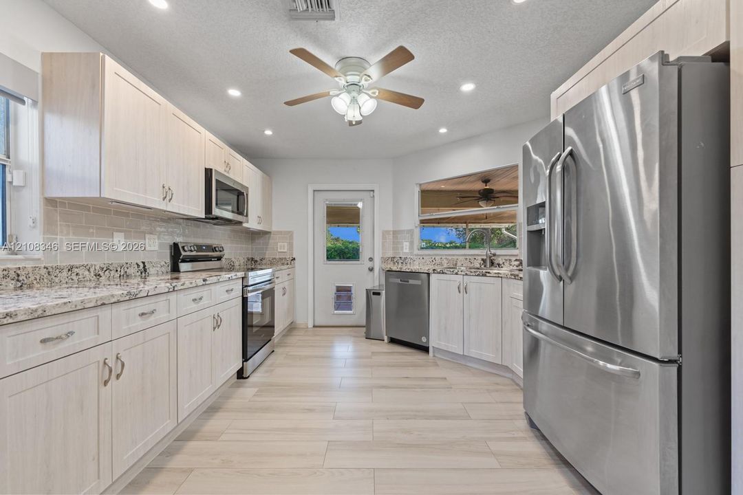 Kitchen featuring light-toned cabinetry, stone-finish countertops, stainless steel appliances, tile backsplash, and wood-tile flooring and exterior door to lani