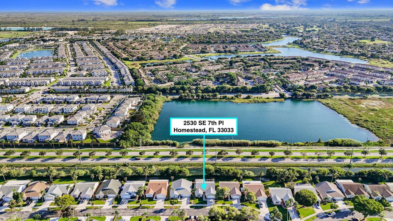 Aerial perspective featuring a single-family residence situated on a lot bordering a large lake with expansive surrounding water features and lush landscaping