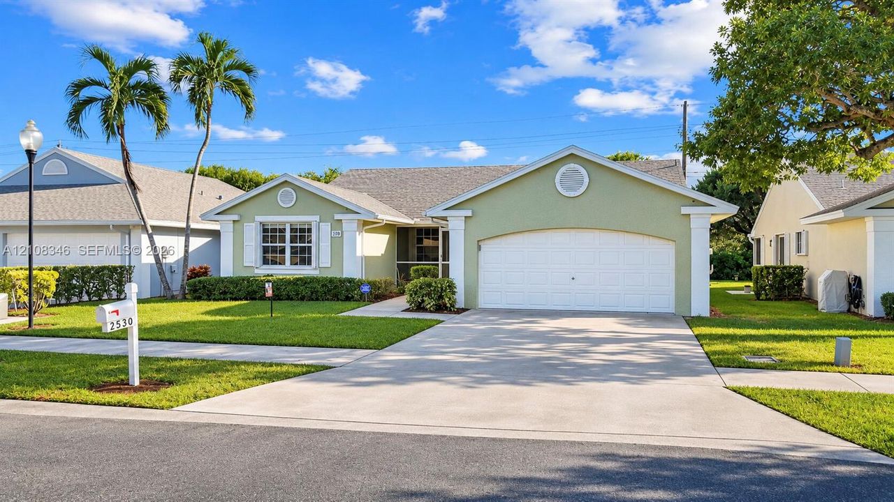 Single-story residence featuring a light green stucco exterior, an arched multi-car garage door, decorative gable vents, and a concrete driveway