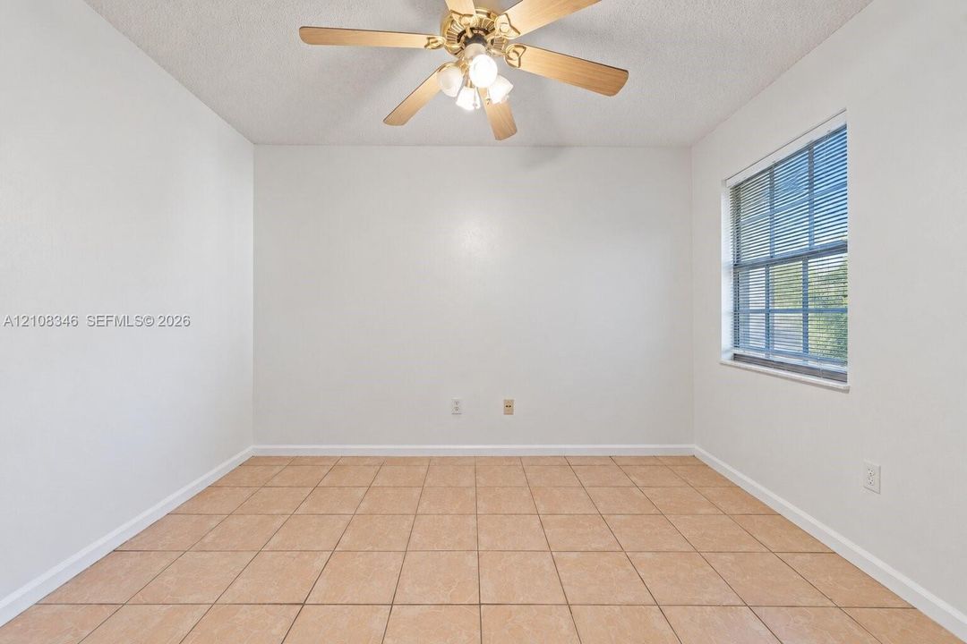 Neutral-toned square tile flooring, light-filled interior with single-pane window, and ceiling-mounted fan with integrated light fixture, closet on opposite wall