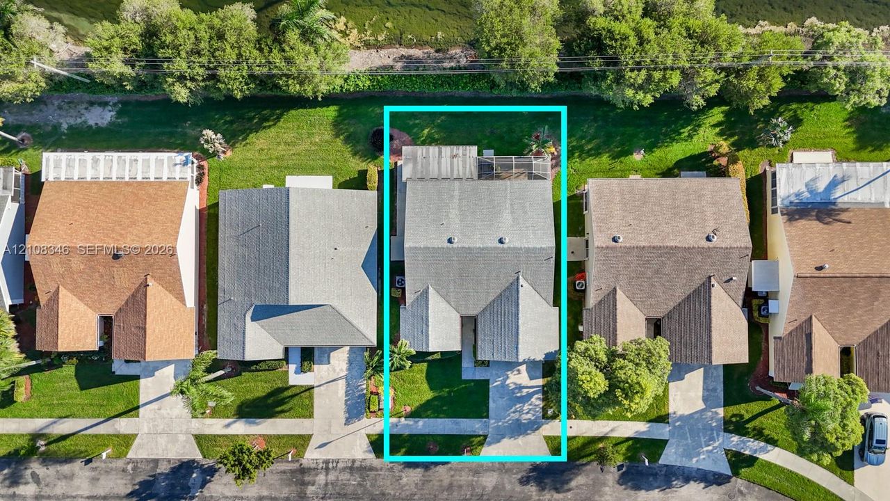Aerial perspective of the property featuring a paved driveway, a multi-gabled roofline, and a rear screened-in enclosure