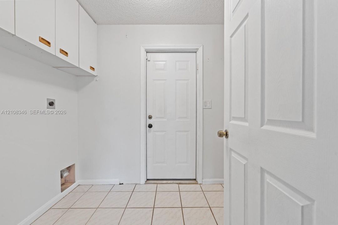 Utility space featuring white wall-mounted cabinetry, tile flooring, and a six-panel exterior door