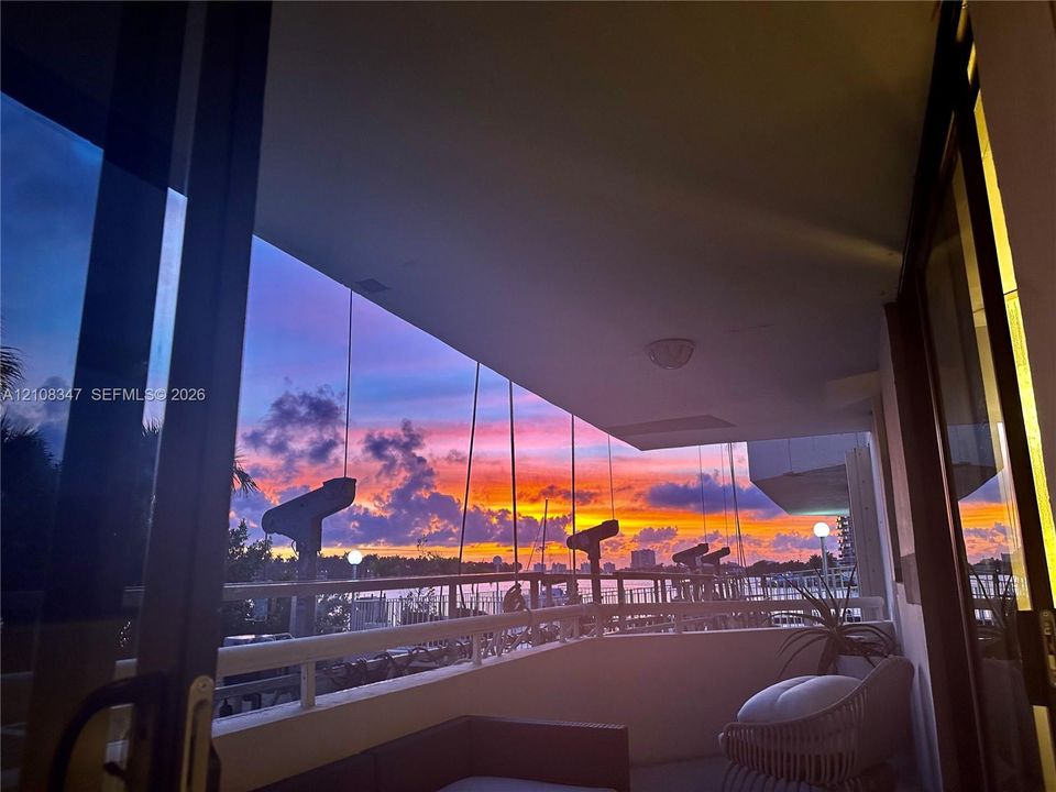 Covered balcony featuring a metal railing and a sunset backdrop over the water