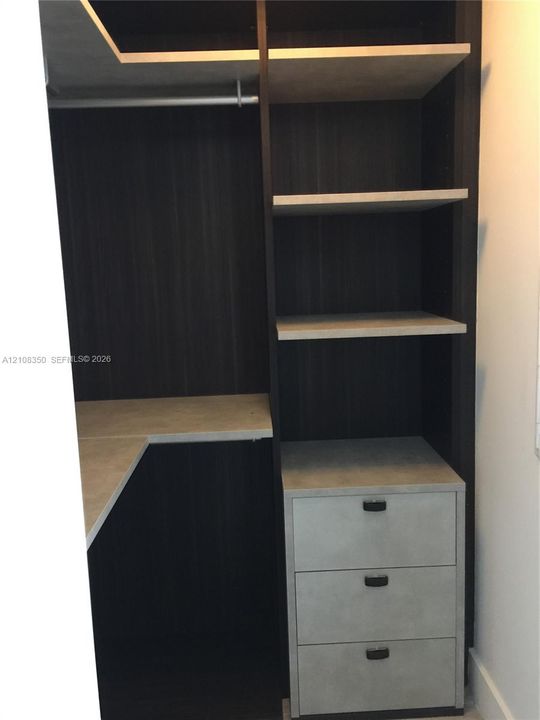Custom built-in storage featuring a dark wood-finish frame, light-toned shelving, three integrated drawers with matte hardware, and a metal garment rod