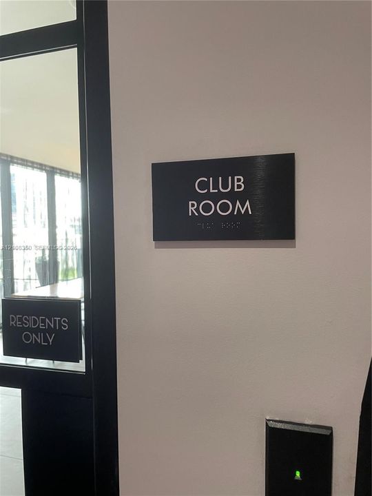 Club room entrance featuring a black signage panel with braille and a secure electronic access control system