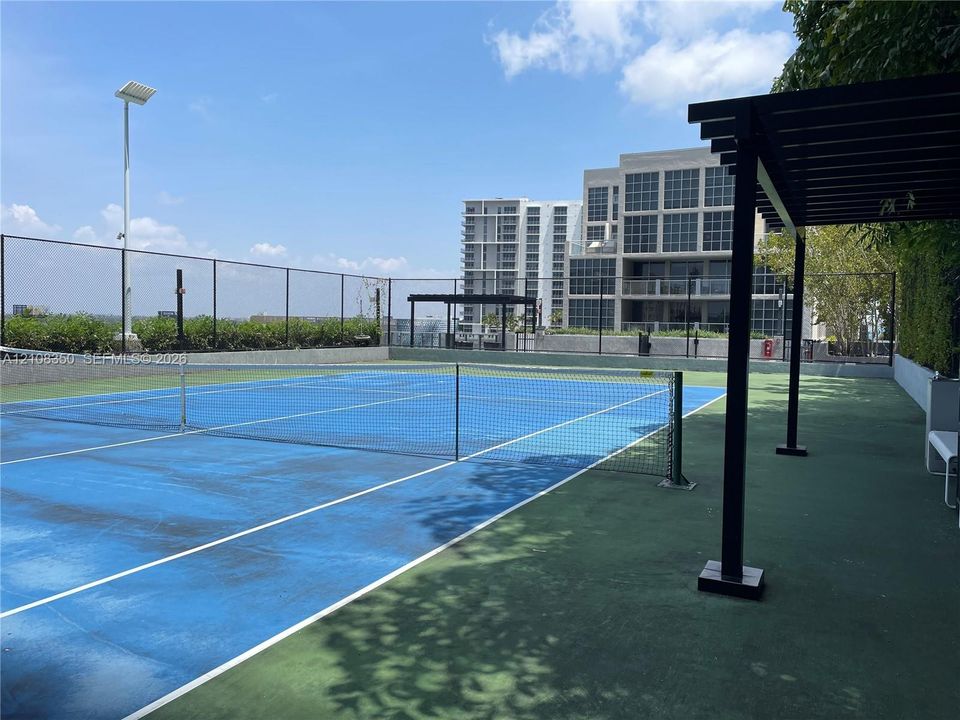 Rooftop tennis court featuring a perimeter fence, overhead lighting, and a metal pergola structure