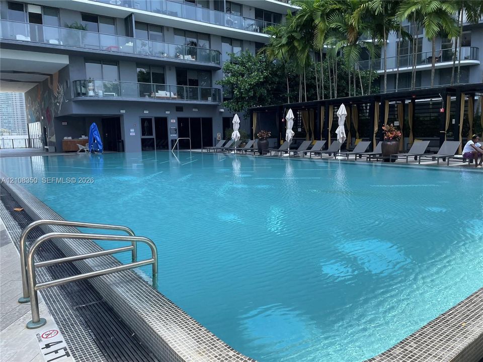 Swimming pool with tile edging, submerged metal ladder, stone pool deck, and covered pergola area