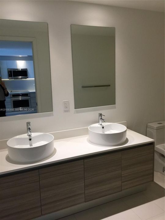 Floating vanity with wood-finish cabinetry, white countertop, dual vessel sinks, chrome faucets, and rectangular wall mirrors